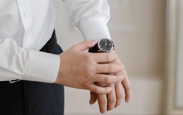 Mann mit Hemd fasst sich an seine Armbanduhr mit durchschnittlichem Durchmesser