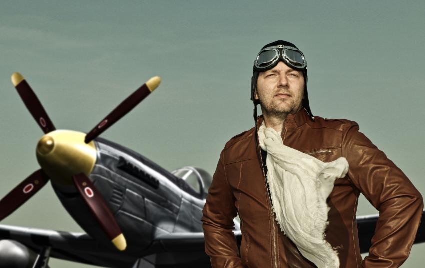 Pilot in Vintage Outfit steht vor historischem Flugzeug