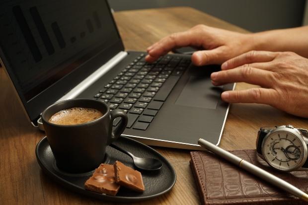 Jemand arbeitet am Laptop, Tasse Kaffee, Armbanduhr liegen daneben, möglicherweise muss man die Uhr entmagnetisieren